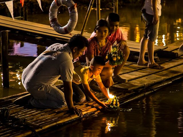 Thai people setting their candle-lit krathongs in the Ping river at night during